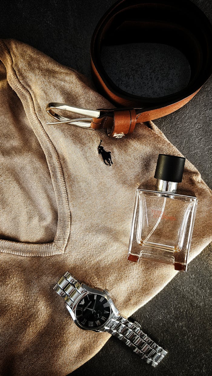 Stylish flat lay of brown sweater, belt, watch, and perfume for men's fashion inspiration.